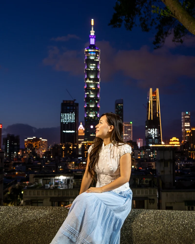 Woman sitting at Huian Park with Taipei 101 in the background in Taiwan